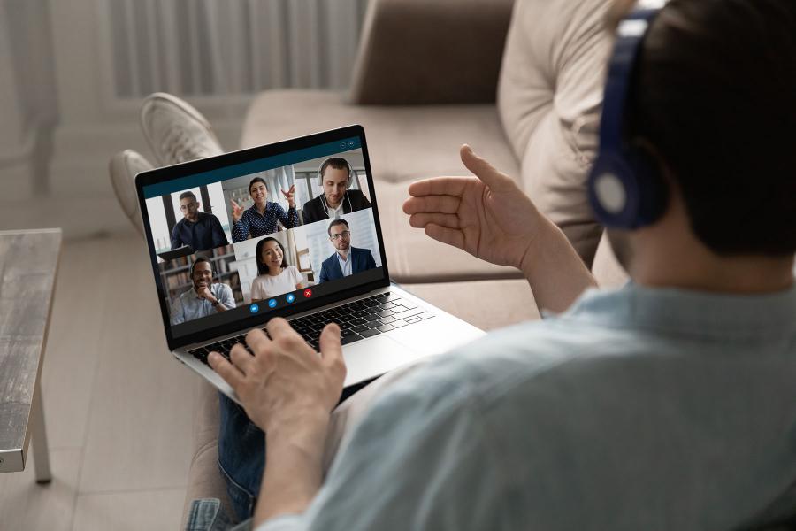 male on sofa, engaged in an online meeting with a diverse group of coworkers