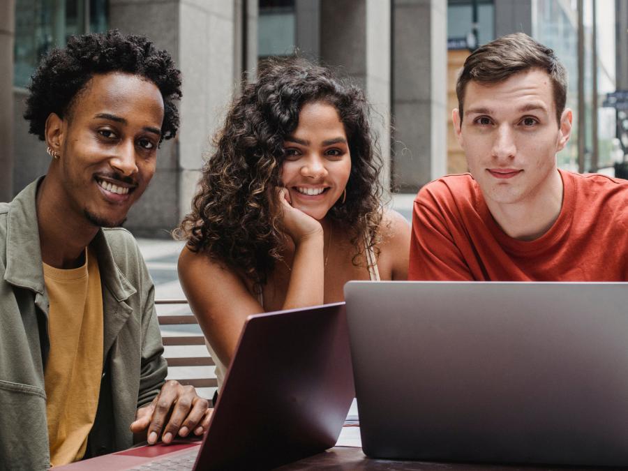 Three students huddled around a laptop at school.